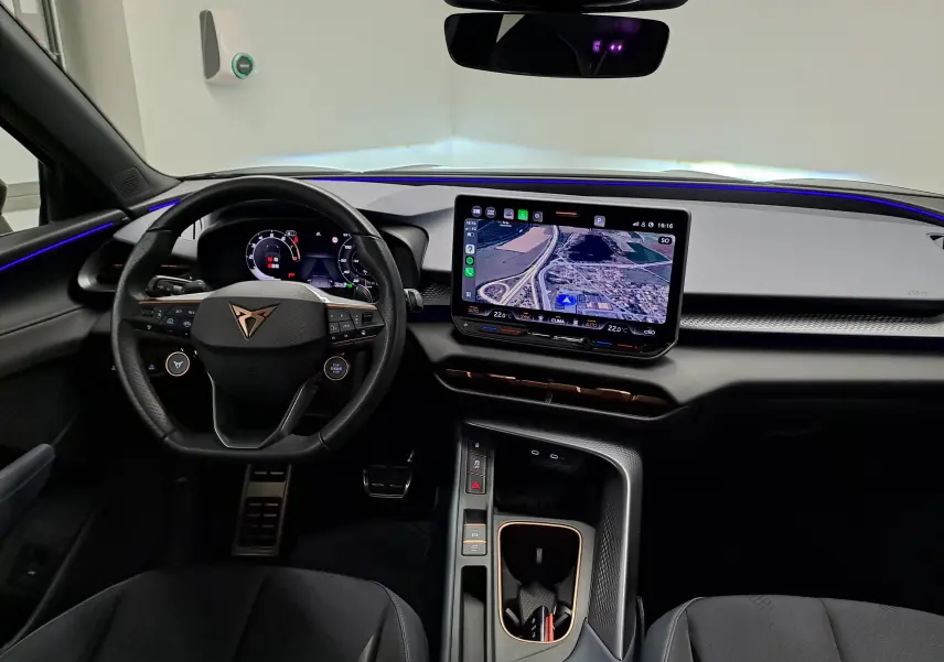 Vue intérieure avant du tableau de bord de la CUPRA TERRAMAR 2025 avec écran tactile central et éclairage d'ambiance bleu.