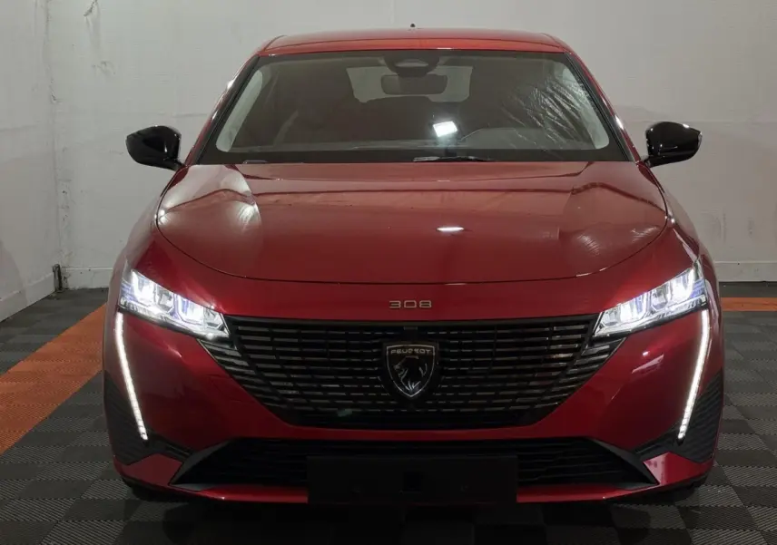 Vue frontale d'une Peugeot 308 rouge 2025 avec phares LED allumés et calandre noire distinctive.