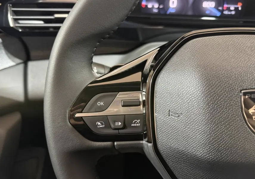 Gros plan sur le volant cuir multifonctions de la Peugeot 308 rouge, avec commandes de régulateur et assistant.