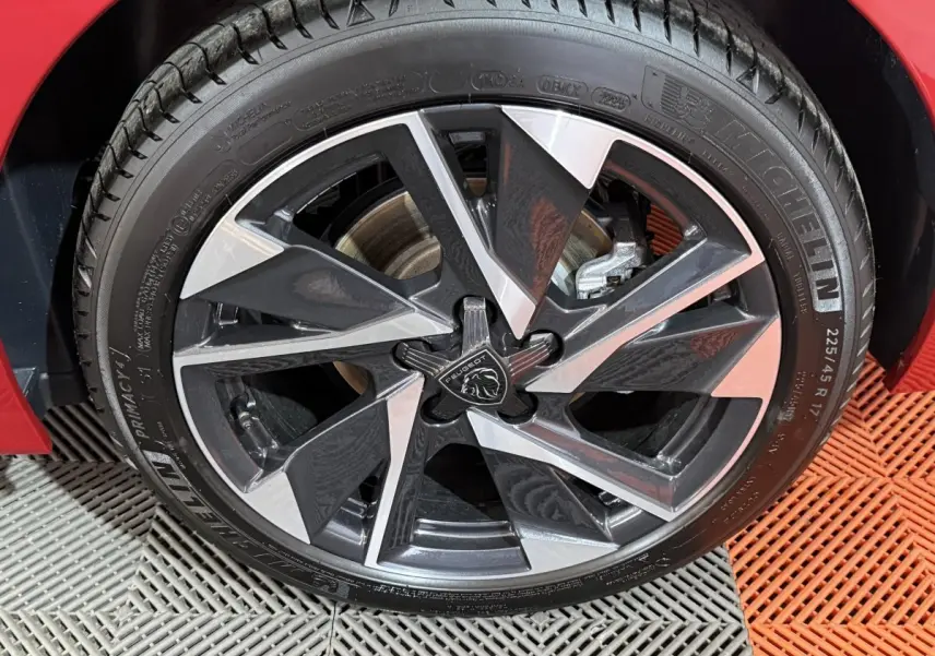 Gros plan sur la jante alliage bicolore et pneu Michelin d’une Peugeot 308 rouge, côté avant droit.