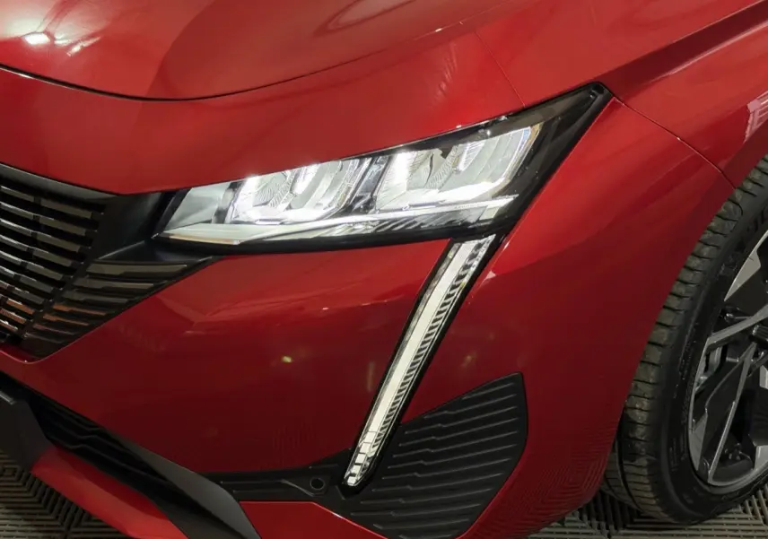 Gros plan sur l'avant droit rouge de la Peugeot 308 2025 avec phares LED et partie de la roue visible.
