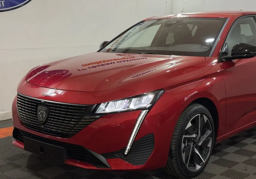 Vue 3/4 avant droit de la Peugeot 308 rouge 2025 avec phares LED et calandre noire distinctive.