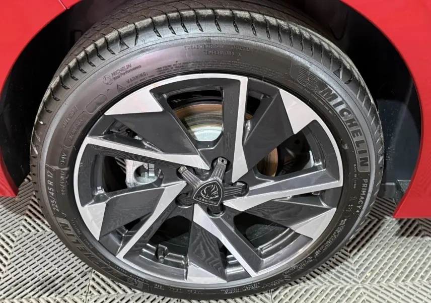 Gros plan sur la roue avant droite de la Peugeot 308 rouge, mettant en valeur la jante alliage bicolore et le pneu Michelin.