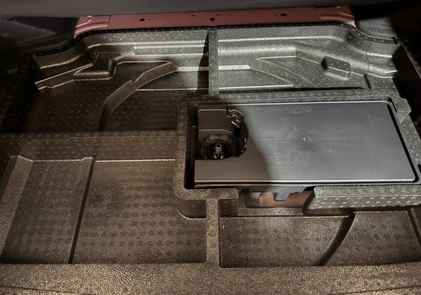 Vue rapprochée du rangement sous le plancher du coffre de la Peugeot 308 rouge, compartiments en mousse noire.