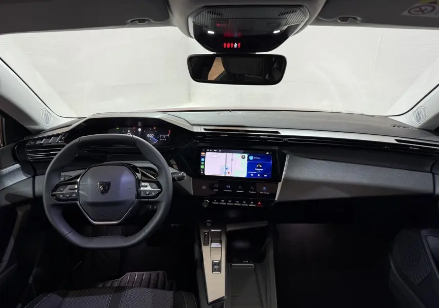 Vue intérieure frontale du tableau de bord et volant cuir multifonctions de la Peugeot 308 2025, écran tactile central allumé.