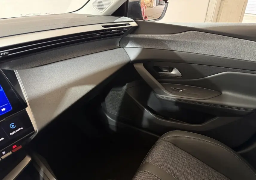 Vue intérieure côté passager du tableau de bord et porte noire de la Peugeot 308 rouge, finition Allure 2025.