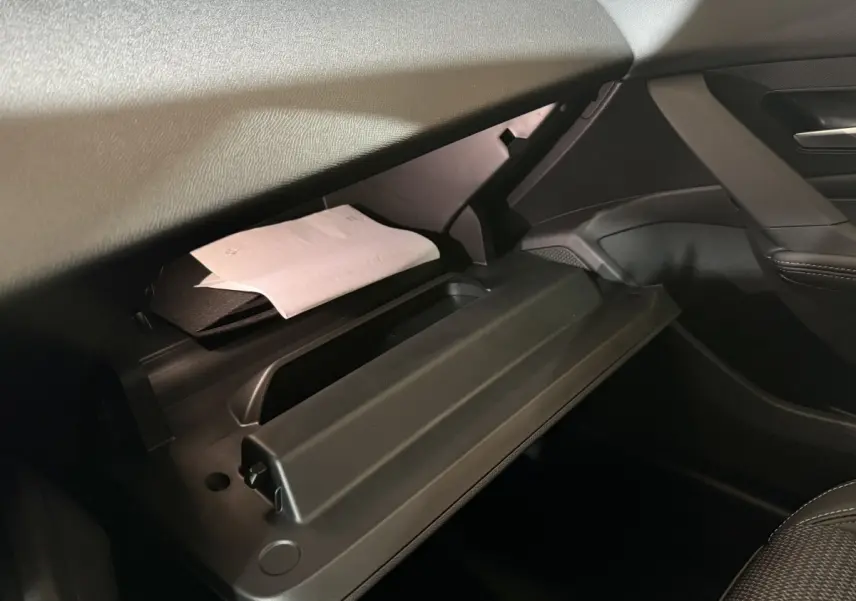 Gros plan sur la boîte à gants ouverte côté passager de la Peugeot 308 rouge, montrant des documents à l'intérieur.