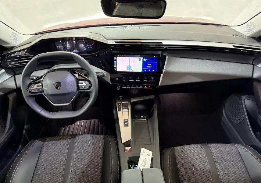 Vue intérieure avant de la Peugeot 308 rouge 2025, volant cuir multifonctions et écran tactile central affichant la navigation.