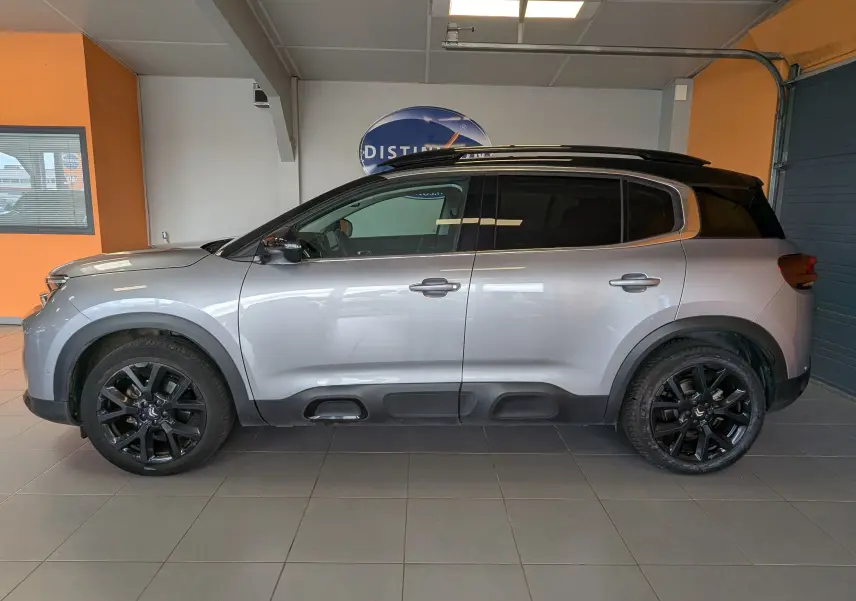Vue de profil côté gauche d'un Citroën C5 Aircross gris Artens avec toit noir et jantes noires en intérieur showroom.