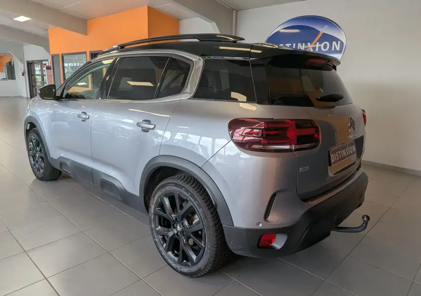 Vue 3/4 arrière droite du Citroën C5 Aircross gris Artens 2024 avec toit noir, jantes noires et attelage visible en intérieur showroom.