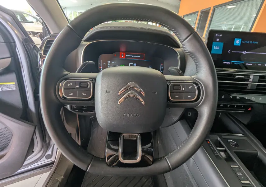 Vue intérieure centrée sur le volant noir du Citroën C5 Aircross 2024 avec tableau de bord numérique et écran tactile.