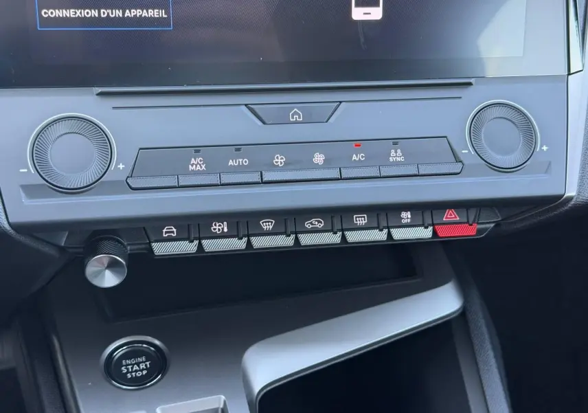 Vue rapprochée de la console centrale de la Peugeot e-308 noire, avec commandes climatisation et bouton start/stop visibles.