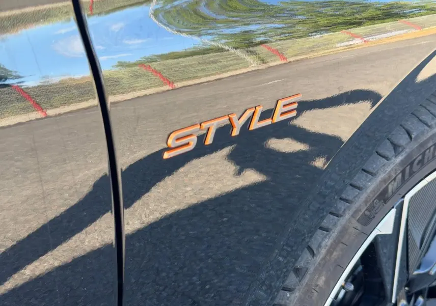 Détail de l’inscription Style orange sur la carrosserie noire Perla Nera d’une Peugeot e-308, près de la roue avant droite.
