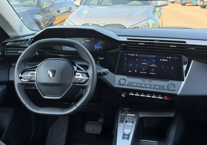 Vue intérieure avant du tableau de bord et volant noir de la Peugeot e-308 2025 avec écran tactile et commandes au volant.