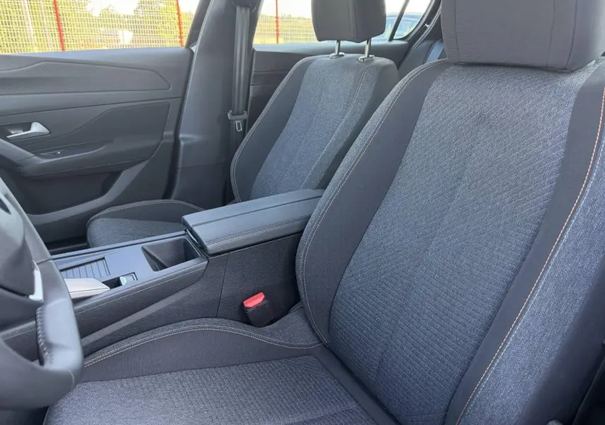 Vue intérieure rapprochée des sièges avant en tissu gris avec surpiqûres orange dans une Peugeot 308 e-308 2025.