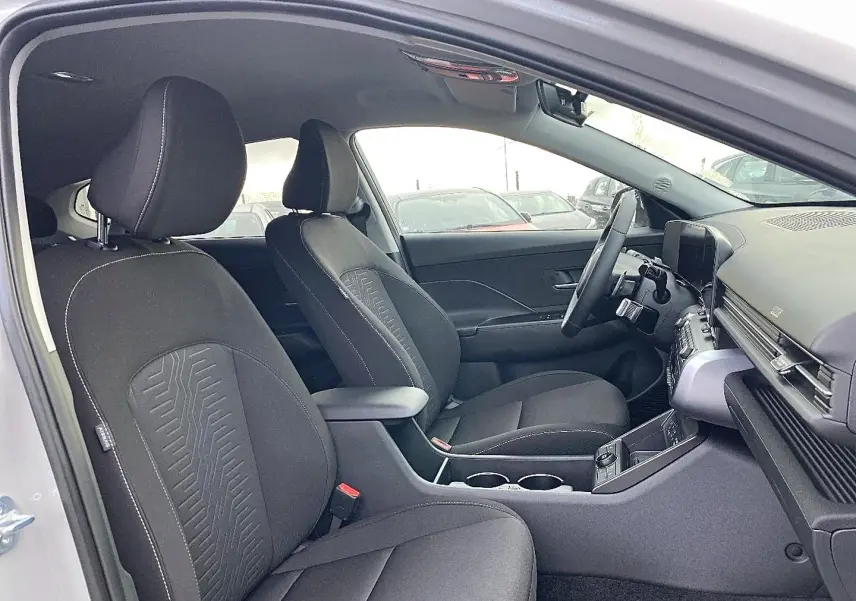 Vue intérieure côté conducteur du Hyundai Kona 2025 gris, montrant sièges avant, volant multifonction et console centrale.