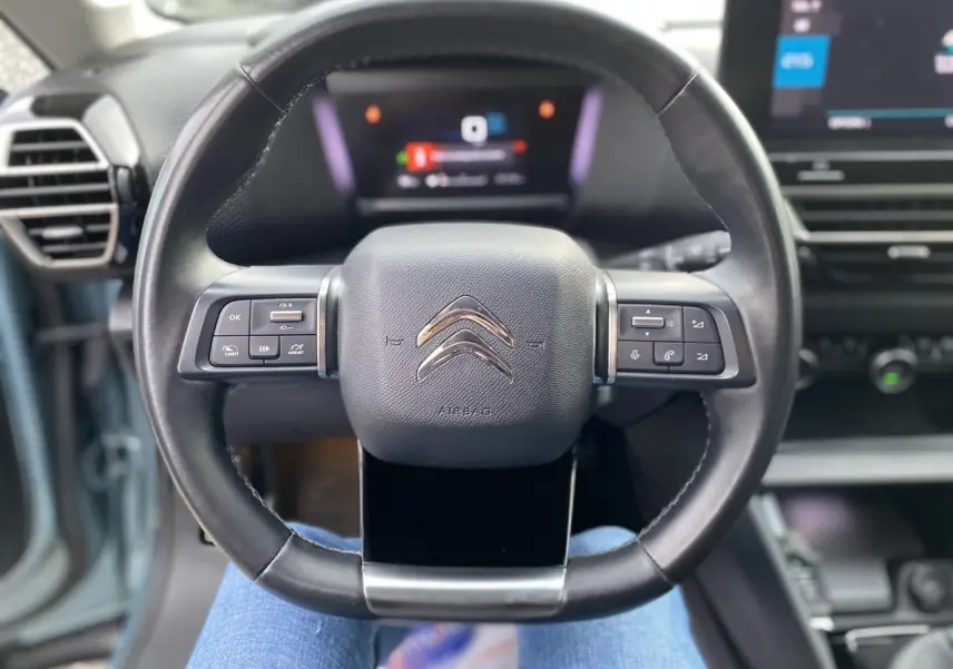 Vue rapprochée du volant cuir noir de la Citroën C4 2021 avec commandes intégrées et tableau de bord numérique flou.