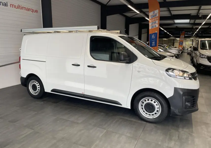 Opel Vivaro blanc en vue de profil côté gauche, fourgon utilitaire avec galerie de toit et jantes tôle.