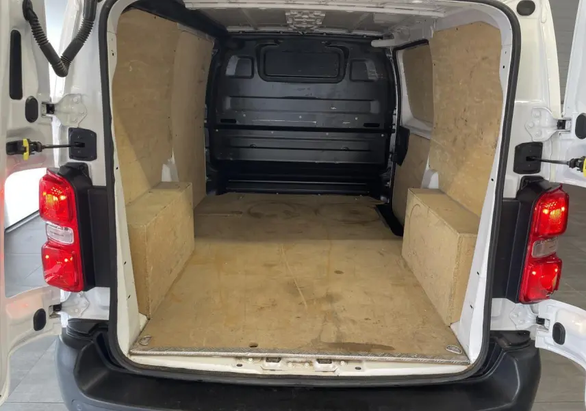 Vue arrière ouverte du fourgon Opel Vivaro blanc montrant l'espace de chargement avec cloison tôlée noire et plancher protégé.