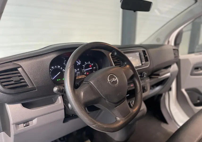 Vue intérieure côté conducteur de l'Opel Vivaro blanc 2021, volant noir avec logo Opel et tableau de bord moderne.