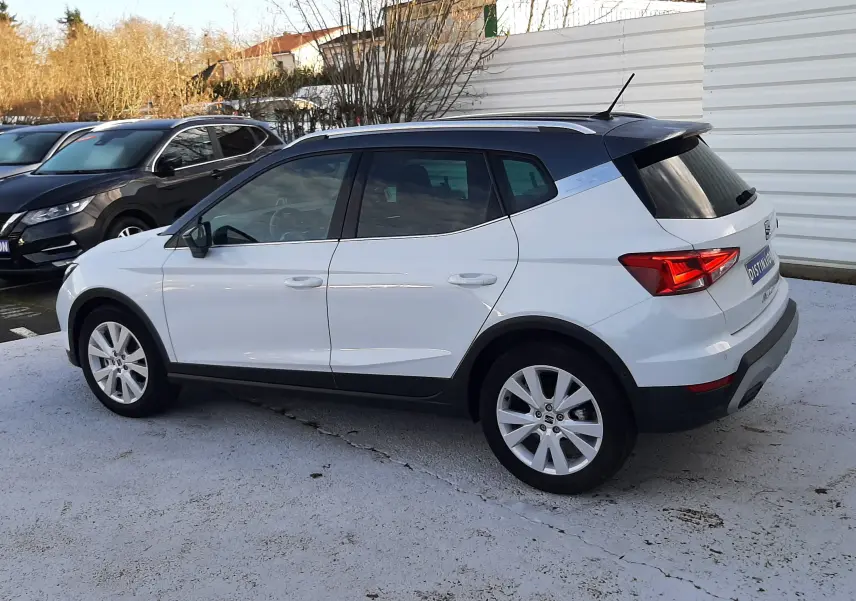 Vue côté gauche arrière d'un SEAT Arona blanc Nevada avec toit gris, soulignant son design compact et ses jantes alliage.