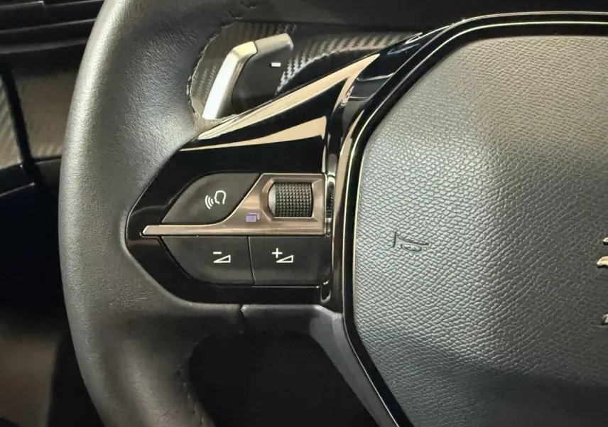 Gros plan sur le côté gauche du volant cuir noir du Peugeot 2008 gris clair, avec commandes multifonctions intégrées.