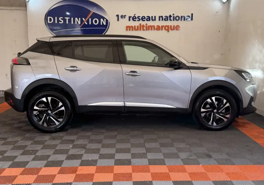 Profil droit d'un Peugeot 2008 gris clair 2023, avec jantes noires et toit noir, stationné en intérieur sur sol damier.