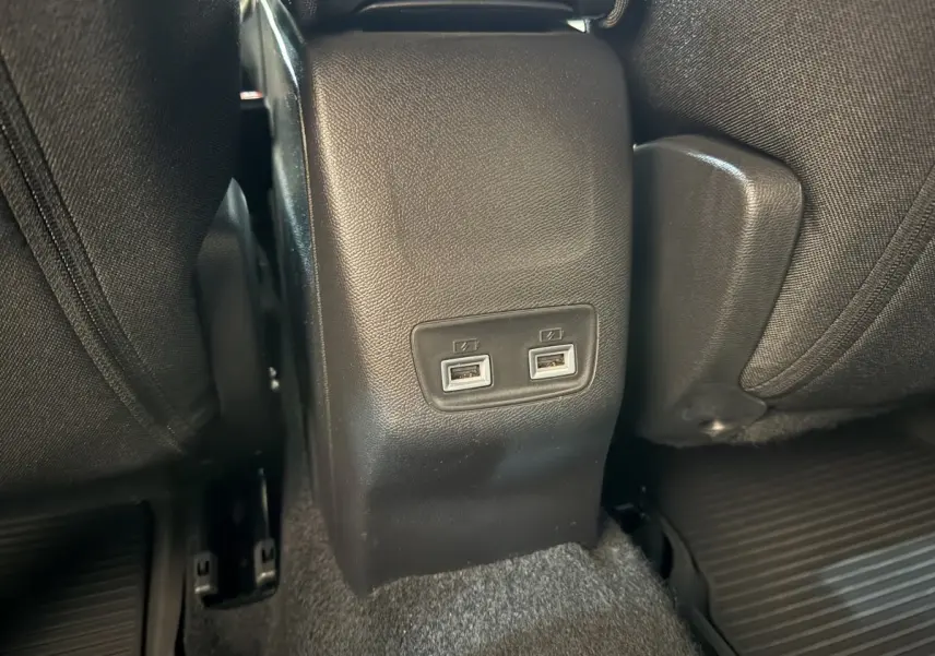 Prise double USB arrière entre les sièges noirs d’un Peugeot 2008 gris clair, vue rapprochée du plancher.