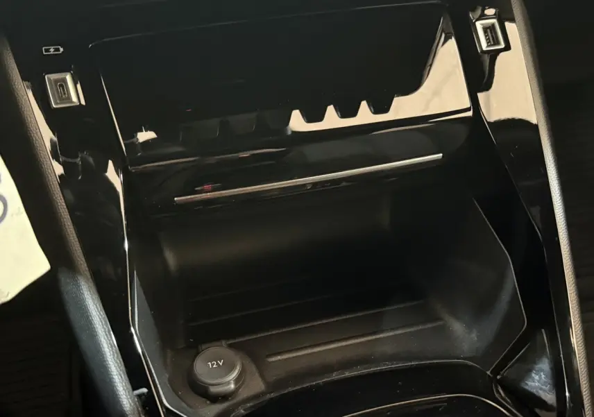 Gros plan sur la console centrale noire brillante du Peugeot 2008 2023 avec prise 12V visible.
