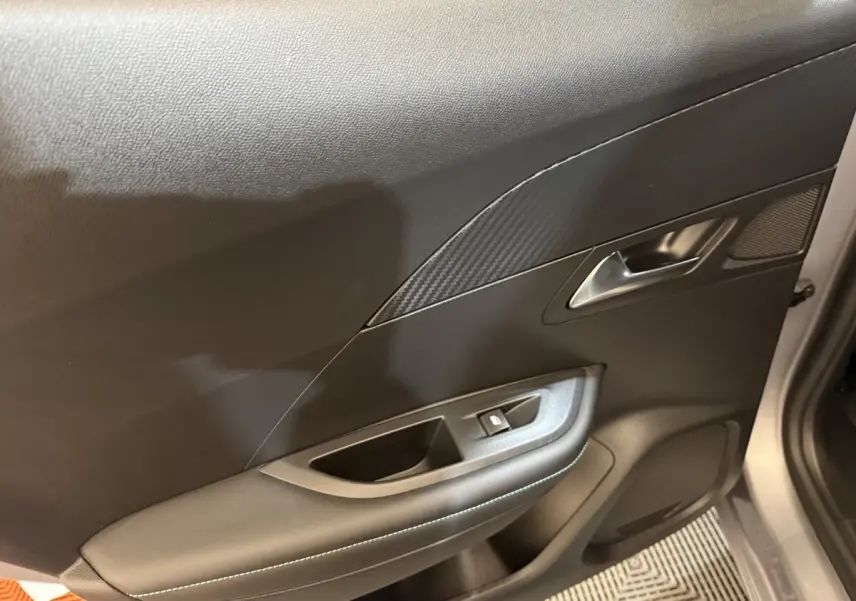 Vue intérieure côté droit de la porte avant grise claire du Peugeot 2008 avec poignée argentée et commande de vitre.