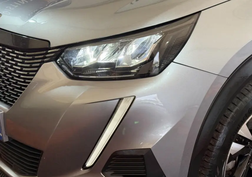 Gros plan sur l'avant droit gris clair du Peugeot 2008 2023, mettant en valeur le phare LED et la calandre distinctive.