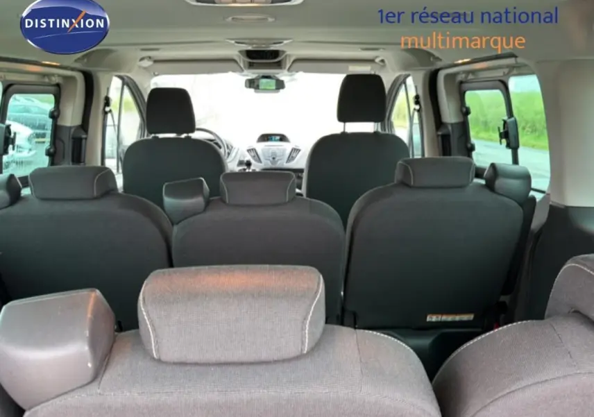 Vue intérieure arrière du Ford Tourneo Custom gris foncé, montrant les sièges passagers et le tableau de bord à l'avant.