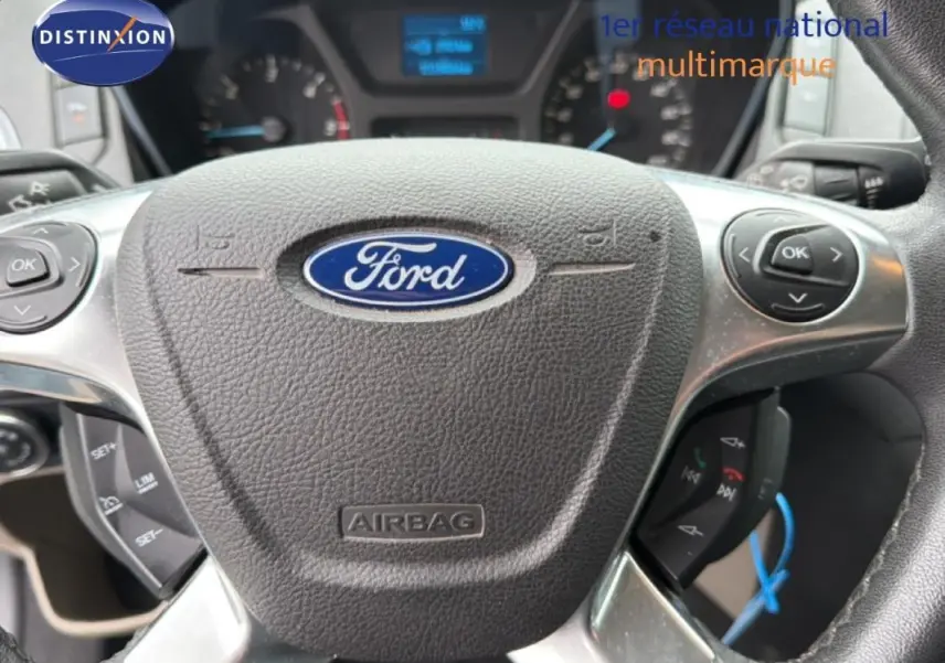 Gros plan sur le volant Ford gris foncé du Tourneo Custom 2015 avec commandes intégrées et tableau de bord flou en arrière-plan.