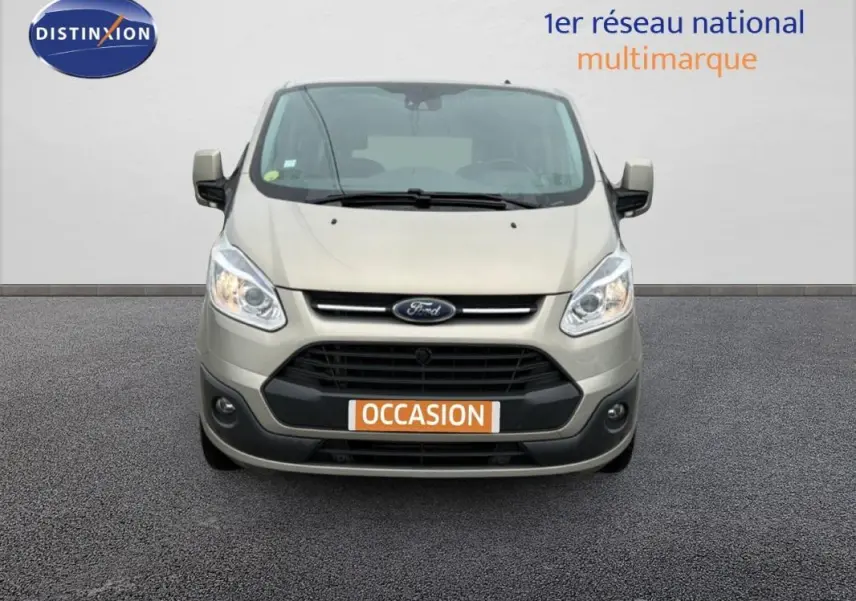 Vue de face d'un Ford Tourneo Custom gris clair avec plaque "OCCASION" et phares allumés sur fond neutre.
