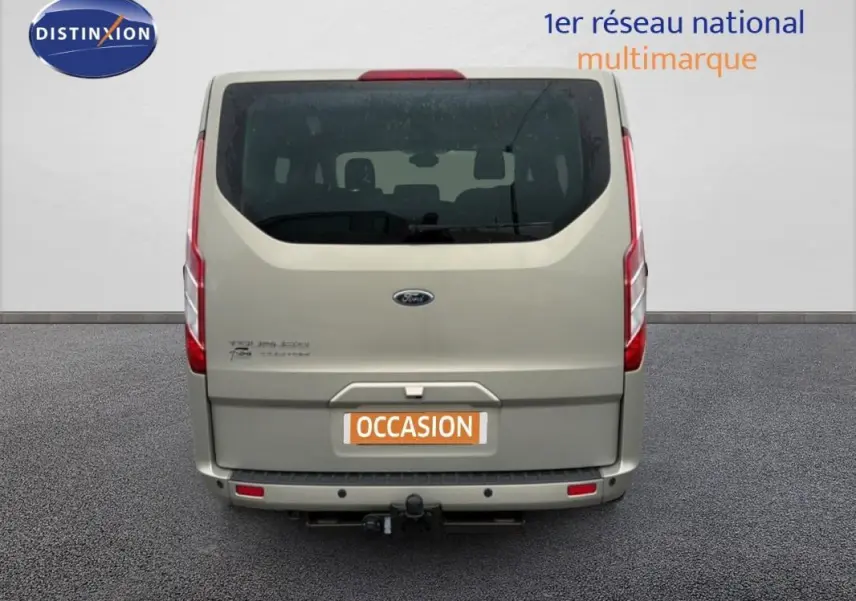 Vue arrière d’un Ford Tourneo Custom gris foncé avec attelage et vitres surteintées, en stationnement sur sol goudronné.