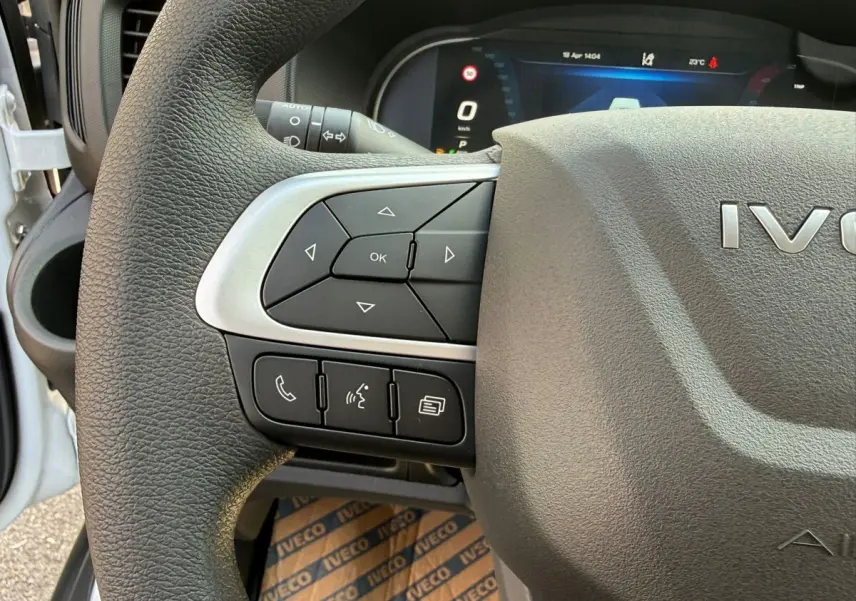Gros plan sur le volant gris foncé de l'Iveco Daily 2026, avec commandes multifonctions et tableau de bord numérique en arrière-plan.