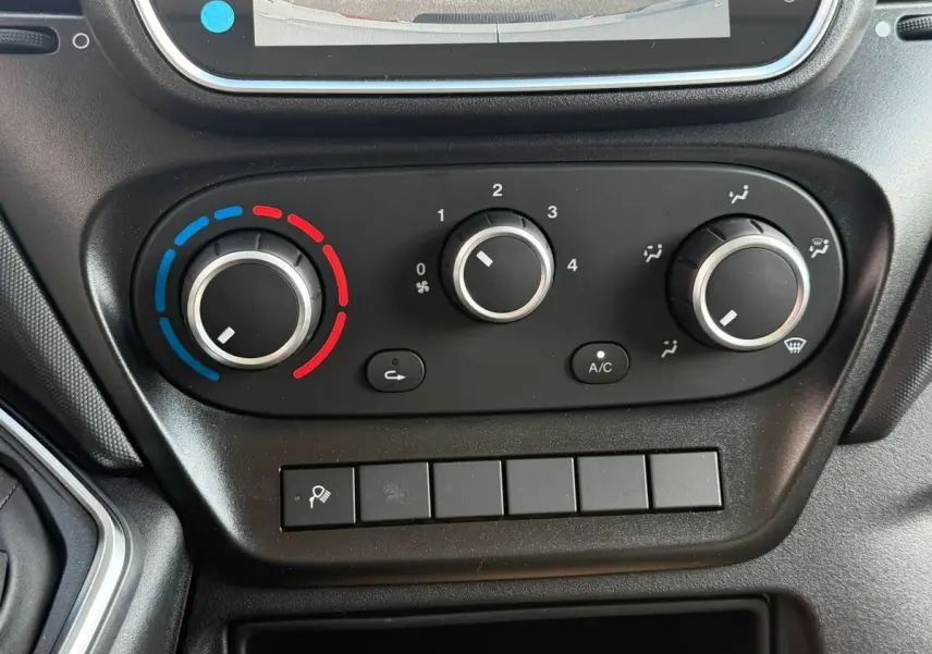 Gros plan sur les commandes de climatisation manuelle du tableau de bord noir du Iveco Daily blanc, version 2026.