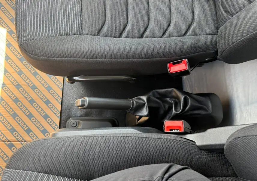Vue plongeante sur la console centrale et les sièges noirs du fourgon Iveco Daily blanc, avec frein à main visible.