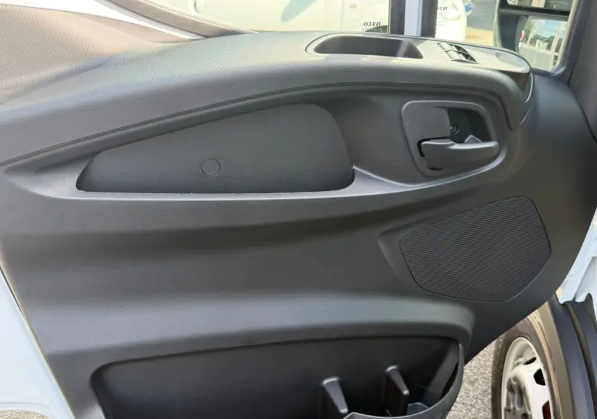 Vue rapprochée de la porte côté droit du fourgon Iveco Daily blanc, montrant la poignée intérieure et le haut-parleur intégré.