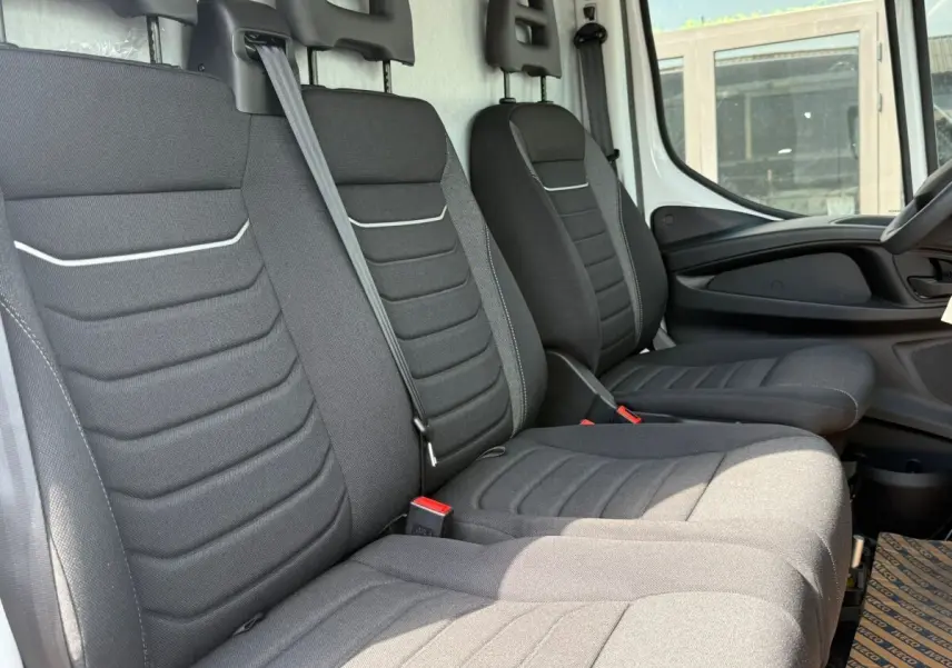 Vue intérieure côté droit montrant les sièges avant noirs du fourgon Iveco Daily blanc, avec ceinture de sécurité centrale visible.