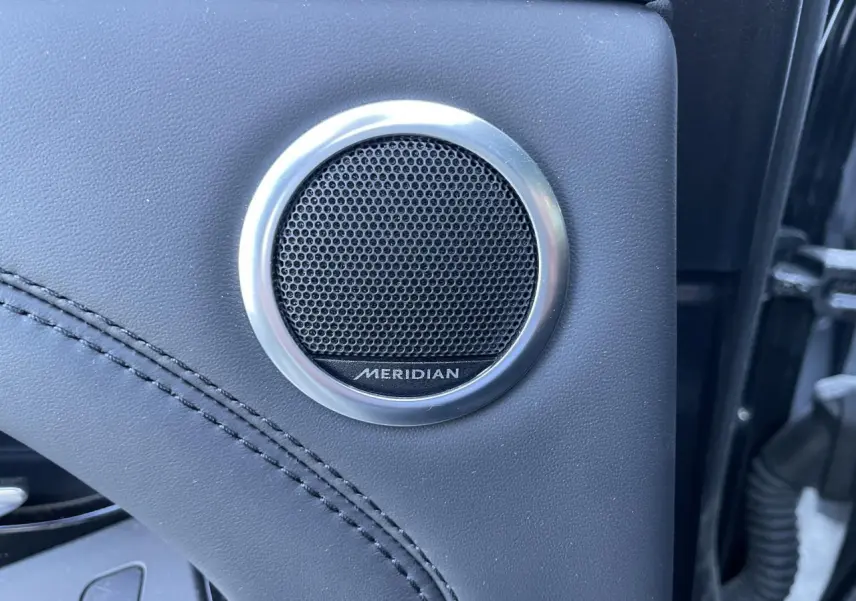 Gros plan sur l'enceinte Meridian intégrée dans la porte en cuir noir du Range Rover Evoque gris 2019.