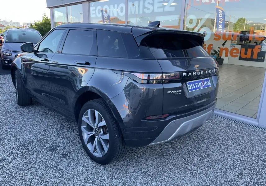Vue 3/4 arrière droite d'un Range Rover Evoque gris métallisé garé devant une vitrine avec logo Distinxion.