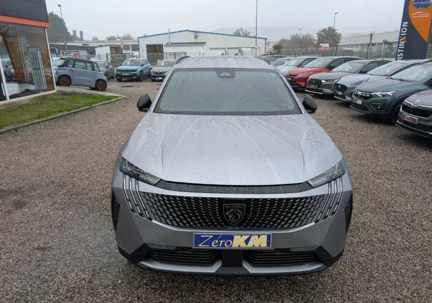 Vue avant d'un Peugeot 5008 gris Artense 2025 avec calandre noire et logo lion central sous la pluie.