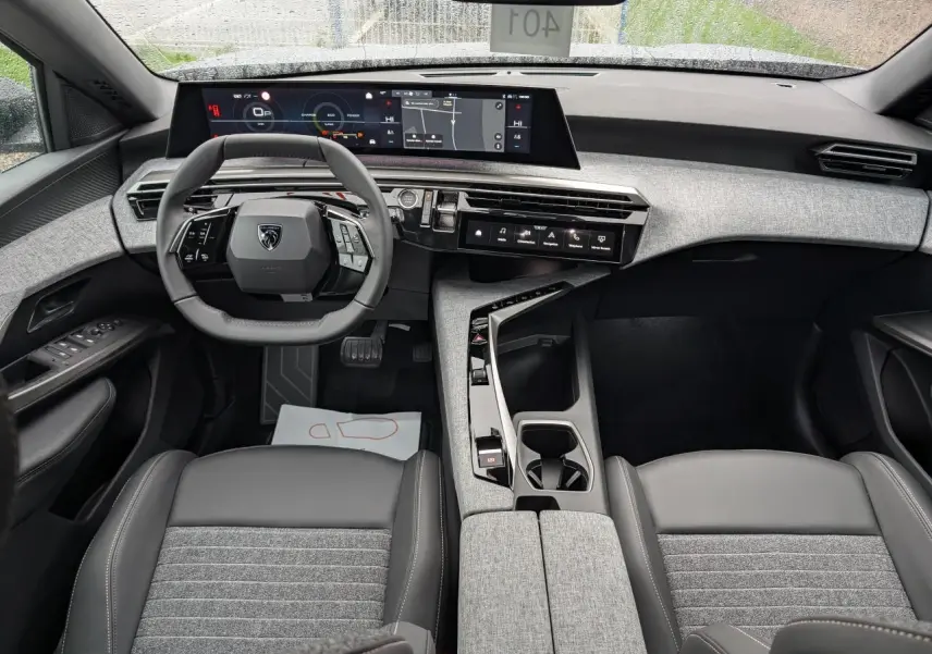 Intérieur du Peugeot 5008 2025 vu de face, avec tableau de bord gris clair et sièges tissu gris foncé.