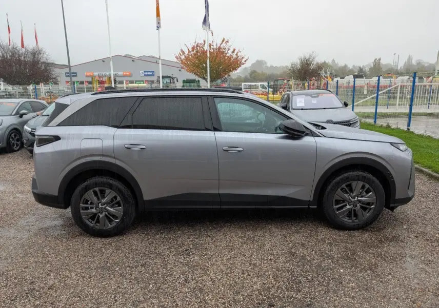 Profil côté gauche du Peugeot 5008 gris Artense 2025 avec jantes alliage et vitres teintées sur parking.