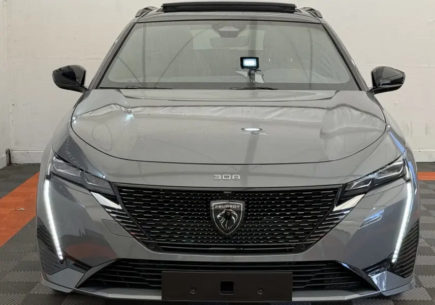 Vue frontale d'une Peugeot 308 Hybrid gris foncé avec calandre noire et feux LED verticaux allumés.