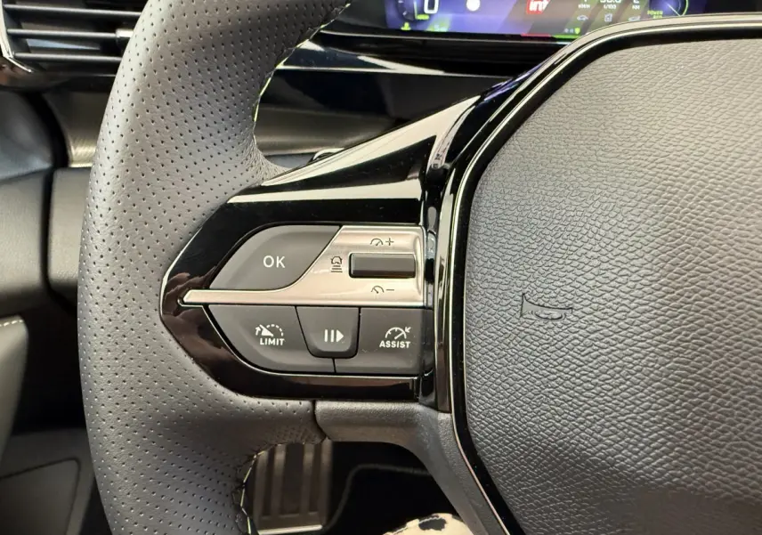 Gros plan sur le volant cuir gris foncé de la Peugeot 308 Hybrid 2024, avec commandes multifonctions et tableau de bord numérique.