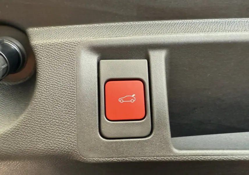 Bouton rouge d'ouverture du coffre sur la garniture intérieure grise d'une Peugeot 308 Hybrid 136 e-DCS6 GT.