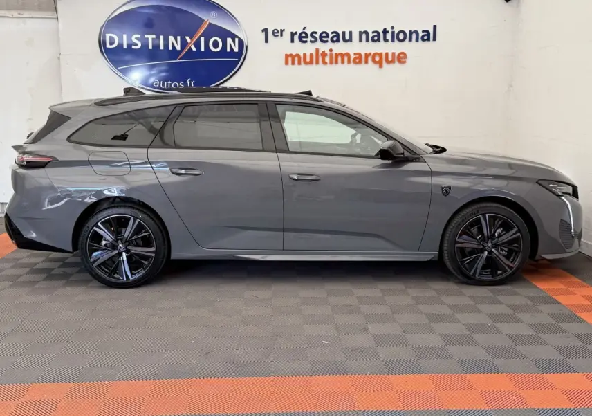 Profil droit d'une Peugeot 308 Hybrid 136 e-DCS6 GT gris foncé, avec jantes noires et toit panoramique visible.