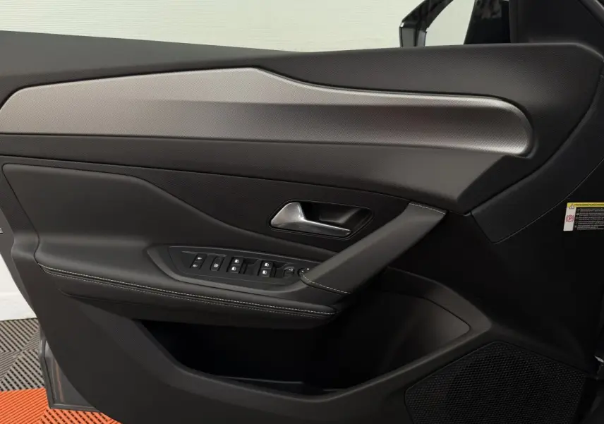 Vue intérieure côté gauche de la porte avant d'une Peugeot 308 Hybrid 136 e-DCS6 GT gris foncé avec commandes de vitres et poignée chromée.